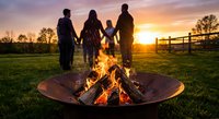 Family holding hands around campfire at sunset in rural countryside with wooden fence and golden sky creating warm bonding moment outdoors.