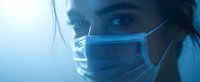 Medical professional wearing protective surgical mask in blue tinted lighting, close-up view showing intense focused eyes and determination during healthcare crisis.