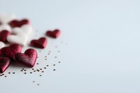 Red glitter hearts scattered on white surface with tiny golden stars, creating romantic Valentine's Day composition with soft focus and copy space.