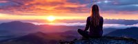 Young Caucasian woman in meditation pose sitting on mountain peak at sunrise, overlooking misty valley with dramatic orange and purple sky panorama.