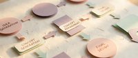 Modern minimalist business cards and branding materials in soft pastel colors scattered on marble surface for corporate identity design projects.