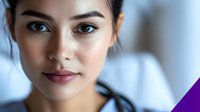 Young Asian woman with natural makeup and glowing skin smiling gently at camera against soft blurred background, beauty and wellness concept.