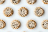 Homemade sesame seed cookies arranged in rows on white background. Golden brown round biscuits topped with white sesame seeds for baking and dessert concepts.