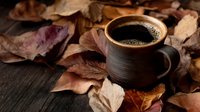 Steaming cup of fresh coffee in rustic ceramic mug surrounded by colorful autumn leaves on dark wooden background, creating cozy fall atmosphere.
