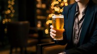 Man in business attire holding beer glass with golden bokeh lights in background, suitable for bar, pub, and beverage advertising campaigns.