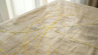 Neutral linen fabric with yellow thread embroidery lines creating abstract geometric patterns, suitable for textile design, home decor, and craft projects.
