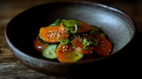 Fresh orange and green tomato salad with sesame seeds and scallions served in rustic ceramic bowl on wooden surface, moody lighting creates appetizing atmosphere.