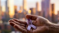 Mature male hands holding small purple gift box against blurred urban skyline at sunset, representing generosity, celebration, and special occasions for greeting cards and holiday marketing.