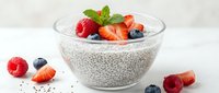 Chia seed pudding topped with fresh berries and mint in glass bowl. Healthy breakfast dessert with strawberries, blueberries, raspberries on white background.