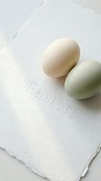 Two pastel Easter eggs in cream and sage green rest on a textured white card with embossed lettering, minimal spring holiday concept.