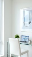 Modern home office workspace with laptop displaying business analytics charts and graphs on glass desk with white chair and plant for remote work productivity.