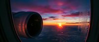 Airplane engine turbine viewed from window during dramatic sunset flight over landscape with golden and purple sky.