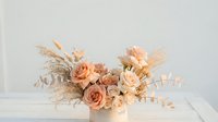 Elegant floral arrangement with peach roses, dried pampas grass, and eucalyptus in a white vase on a rustic table, soft neutral tones.