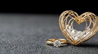 Golden engagement ring with sparkling diamond beside elegant wire heart decoration on dark textured surface for romantic wedding concepts.