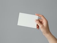 Hand holding blank white card against neutral gray background, ready for custom branding or messaging. Suitable for business cards, invitations, promotional materials, and design mockups.
