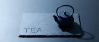 Traditional cast iron teapot on dark slate board with TEA inscription, moody blue tones, elegant minimalist composition for cafe menu.