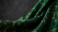 Green fabric with golden embroidered swirls and decorative stitching creates elegant textile pattern for luxury fashion and interior design projects.