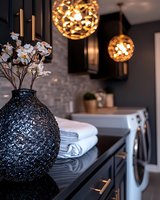 Modern laundry room interior with textured black vase, white orchids, and decorative sphere pendant lights against dark walls and white appliances. Luxury home design.