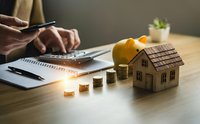 Real estate investment planning with wooden house model, coins, calculator and paperwork on desk for mortgage and property finance decisions.