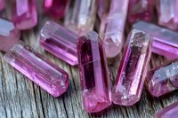 Pink tourmaline crystal specimens on weathered wood surface showing natural mineral formation with translucent properties and prismatic shapes in macro view.