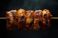 Grilled chicken yakitori skewers with caramelized soy glaze and charred edges on wooden stick against dark background, close up view of traditional Japanese cuisine.