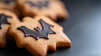 Homemade ginger cookies decorated with dark chocolate bat shapes for Halloween celebration on dark background, selective focus on foreground cookie.