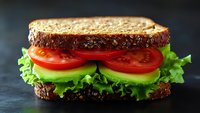 Fresh sandwich with whole grain bread, crisp lettuce, ripe tomato slices and avocado on dark background, appetizing close up view for menu or recipe blog.