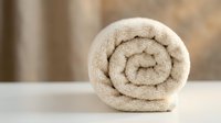 Soft rolled beige towel on white surface with blurred warm background, evoking spa, wellness, and hotel bathroom luxury concepts.