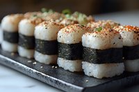 Fresh sushi rolls with rice and nori seaweed arranged on black stone plate, garnished with sesame seeds and green onions, close-up view in natural lighting.