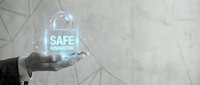 Safe innovation concept with glowing holographic shield symbol held in businessman hand against abstract geometric background, representing data protection and secure technology solutions.