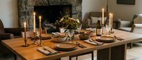 Elegant dining table set with wooden surface, place settings, candles, and floral centerpiece near fireplace for formal dinner entertaining.