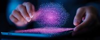 Glowing pink particle cloud floating above digital tablet screen with hands interacting in dark environment, representing digital transformation and technology.