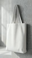 White cotton tote bag hanging on concrete wall with natural lighting for eco-friendly shopping and sustainable lifestyle branding mockup.