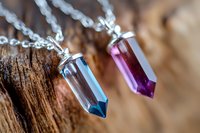 Colorful crystal pendant necklaces on silver chains displayed on natural wood surface for jewelry and fashion accessories.