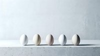 Five white eggs arranged in row on marble surface against textured wall background for cooking baking kitchen design concepts.
