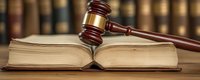 Wooden judge gavel resting on open law book against blurred background of legal library shelves, symbolizing justice system and court proceedings.
