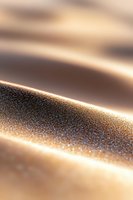 Glittering golden sand dunes with morning light creating dramatic shadows and sparkles on textured surface, macro photography showing fine granular details.