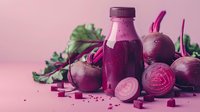 Fresh beetroot juice in glass bottle with raw beets, sliced pieces and green leaves on pink background. Natural detox drink and healthy food concept.