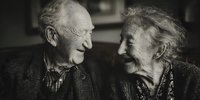 Elderly couple sharing intimate moment together, black and white portrait of senior man and woman looking at each other with love and tenderness in home setting.