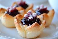 Mini pastry cups filled with dark chocolate ganache and topped with sugar-dusted fresh raspberries on white plate, close-up view of delicate dessert appetizers.