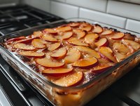 Fresh peach slices arranged in rows atop caramelized brown sugar and butter in glass baking dish, creating traditional upside-down cake before baking.