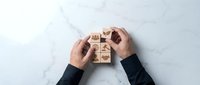 Business strategy concept with hands arranging wooden blocks showing icons for teamwork, leadership, and corporate planning on marble surface.