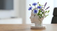 White human head silhouette with purple wildflowers growing from brain area on wooden desk, mental health awareness concept for World Mental Health Day.