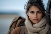 Young Hispanic woman with natural makeup wearing beige scarf and coat outdoors on windy autumn day, close up portrait with soft bokeh background.