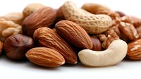 Mixed nuts collection including almonds, cashews, walnuts, and peanuts on white background, macro close up view showing texture and detail. Healthy protein-rich snack.