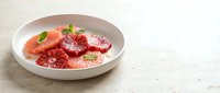 Sliced grapefruit and strawberries arranged in white bowl on marble surface, fresh citrus fruit for healthy breakfast or dessert preparation.
