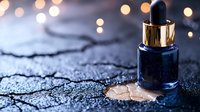 Luxury serum bottle with golden dropper on textured dark surface with warm bokeh lights creating elegant cosmetic product photography for skincare branding.
