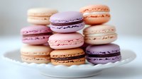 Colorful French macarons in pastel pink, purple, peach and cream shades stacked on white plate, sweet meringue sandwich cookies with filling for dessert menu.
