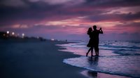 Romantic couple silhouette dancing on beach at sunset with purple sky and ocean waves creating intimate moment for wedding anniversary celebration.