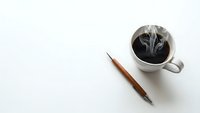 Coffee cup with steam and wooden pen on white desk surface for morning productivity and creative writing workspace setup.
